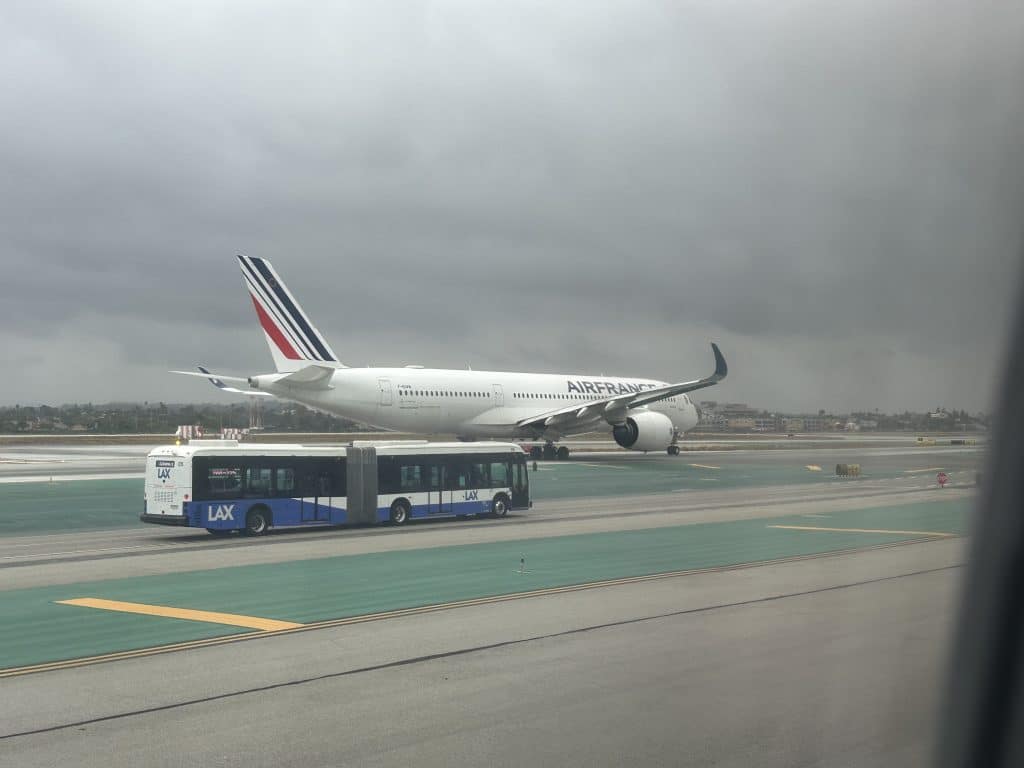 Air France A350 taxiing at LAX with LAX airport shuttle bus in foreground under overcast skies.