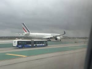 Air France A350 taxiing at LAX with LAX airport shuttle bus in foreground under overcast skies.