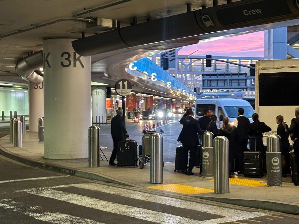 Delta crew waiting outside LAX Terminal 3 near shuttle pickup zone at sunset.