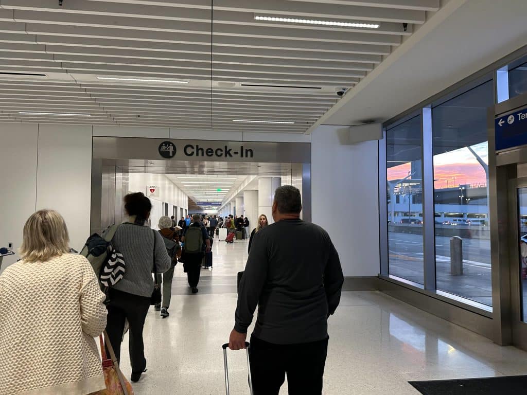 Interior check-in walkway at LAX Terminal 3 with passengers and sunrise view.