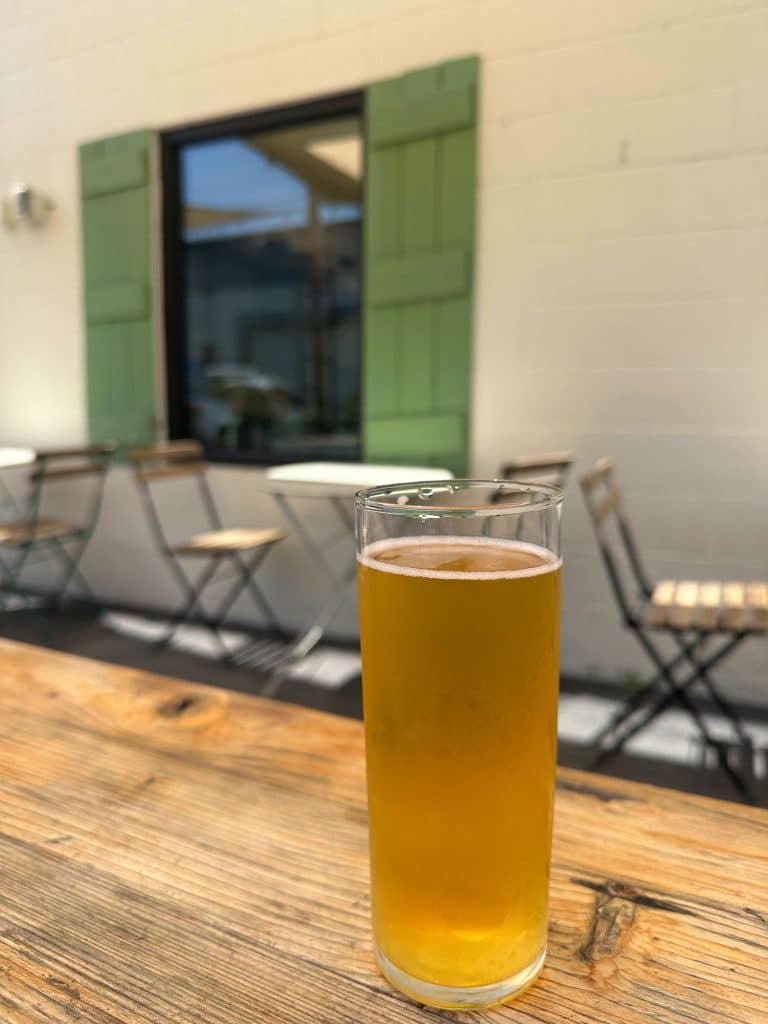Glass of craft IPA beer on a rustic wooden table at Homage Brewing patio in Los Angeles.